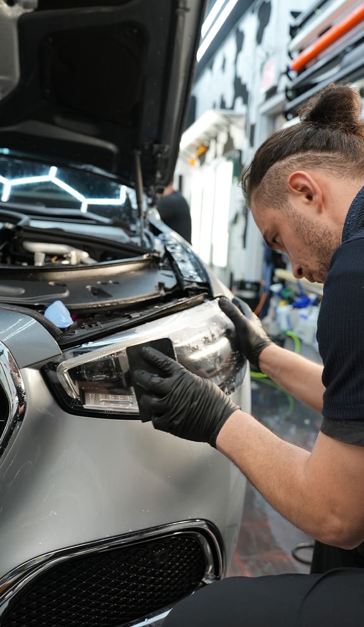 Technician applying STEK Paint Protection Film to car headlights at Grand Prix Customs in Brooklyn, NY